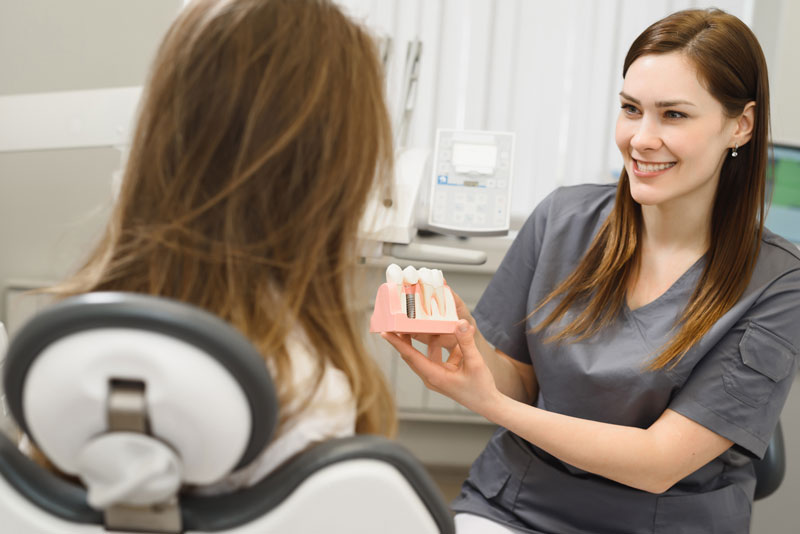 a patient being shown a dental implant model by an oral surgeon as she explains what will happen during her dental implant procedure.