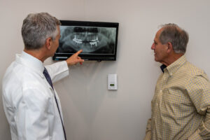 Dr. Casadaban pointing at an x-ray of a patients oral structures as he talks to him about upgrading his smile with implant supported dentures.